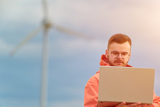 Worker standing with laptop by wind turbine