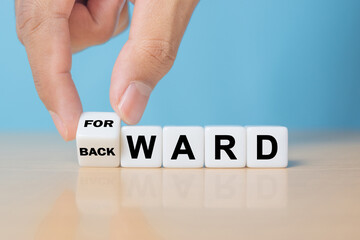 Hand turns a cube and changes the word 'backward' to 'forward' on dice. Beautiful yellow table, white background, copy space.