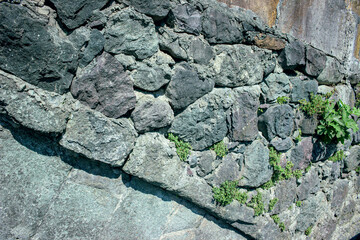 Stone wall made of large gray boulders with green plants