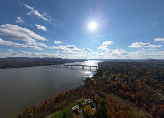 Obraz premium Aerial view of Hudson River with strong sunlight reflecting off the water near Newburgh, NY, showcasing surrounding autumn foliage and deep blue skies. Travel photography.