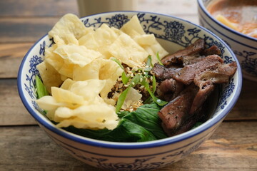 Delicious Asian-style rice bowl topped with grilled beef slices, fresh vegetables, sesame seeds, and crispy crackers in a patterned bowl.
