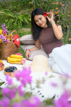 Relaxed young woman enjoying a colorful outdoor picnic in nature with fruits and flowers.