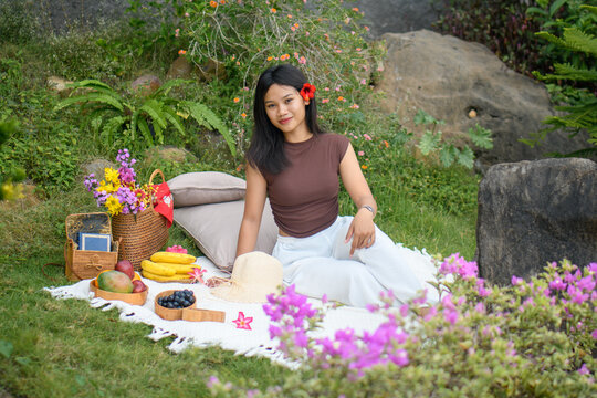 Relaxed young woman enjoying a colorful outdoor picnic in nature with fruits and flowers.