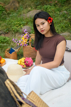 Relaxed young woman enjoying a colorful outdoor picnic in nature with fruits and flowers.