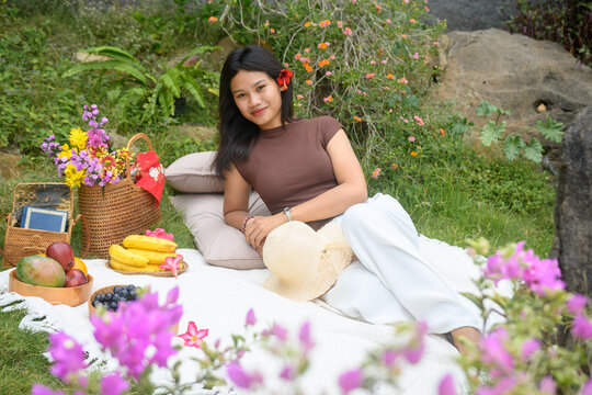 Relaxed young woman enjoying a colorful outdoor picnic in nature with fruits and flowers.