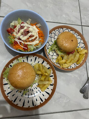 A homemade meal of two hamburgers with french fries and a side salad served on decorative plates and a bowl.