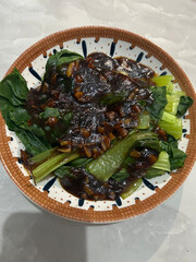 A delicious dish of blanched bok choy greens served in a patterned bowl and topped with a savory dark garlic sauce.
