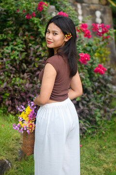 Young woman standing in a garden with a woven bag full of colorful flowers.