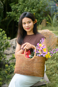 Young woman standing in a garden with a woven bag full of colorful flowers.