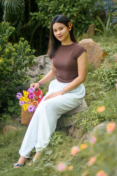 Young woman standing in a garden with a woven bag full of colorful flowers.