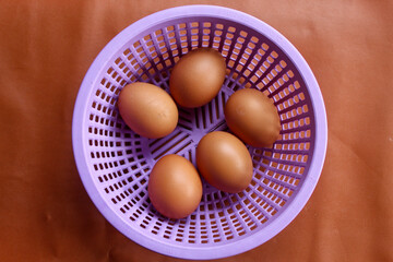 five brown chicken eggs placed in a purple plastic basket with holes