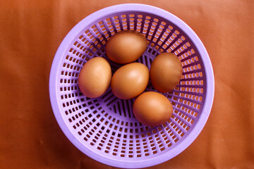 five brown chicken eggs placed in a purple plastic basket with holes