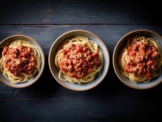 Three bowls of spaghetti with meat sauce, arranged on a dark wooden surface