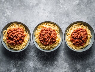 Three bowls of spaghetti with meat sauce, arranged in a row on a mottled gray surface