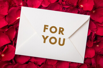White envelope with gold for you text on red rose petals background