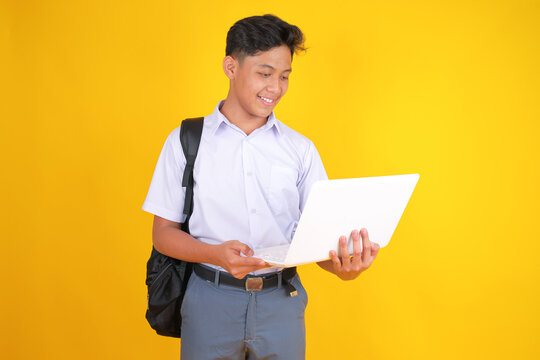 Smiling Student Uses Laptop Eager to Learn and Connect in Classroom or Library on Yellow Backdrop