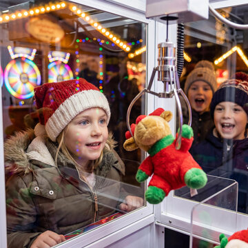 Joyful Kids Enjoy Claw Machine Game At Festive Arcade With Christmas Lights