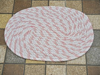 Round handmade doormat made from woven recycled fabric on a ceramic tile floor. Creative handicrafts for household items.