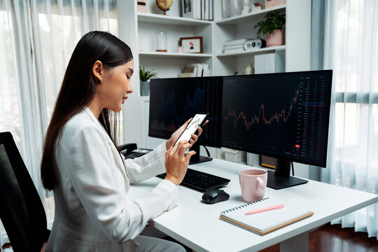 Smiling young Asian businesswoman with happy face looking on smartphone in profitable of exchange stock market graph at modern office. Concept of investing high profit in wealth security. Stratagem. - Powered by Adobe