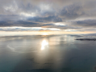 Aerial view of the immense surface of a large inland lake with the sun reflecting brightly, framed by dark, textured clouds above the horizon