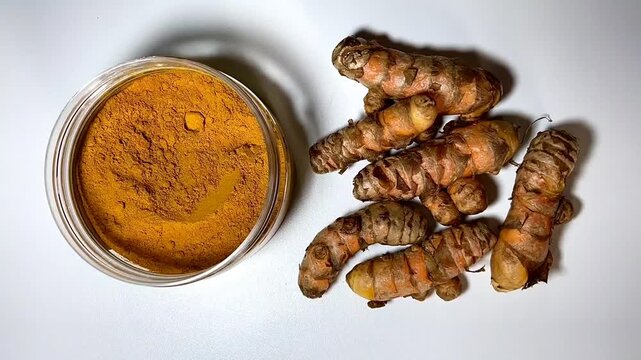 Aromatic turmeric powder and raw roots on white background.