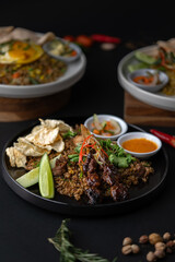 Gourmet Nasi Goreng (Indonesian Fried Rice) with Chicken Satay, Served Elegantly on a Dark Plate in a Restaurant Setting