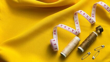 Threads, a measuring tape, and accessories against a yellow background. Concept: clothing repair, home workshop, practicality.