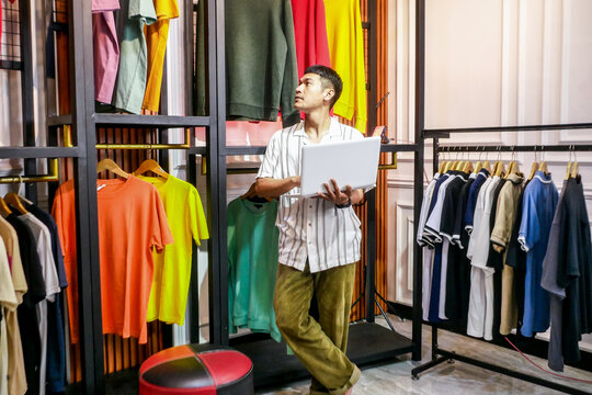 Modern Entrepreneur Analyzes Retail Inventory on Laptop Amidst Vibrant Clothing Racks