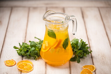Refreshing citrus lemonade with mint leaves and ice served in a clear glass pitcher on a wooden table