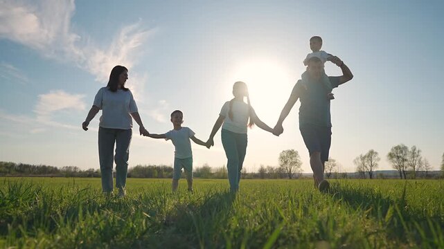 Toddler daughter join family walk. Open grass under setting sun. Holding hands across field. Sunset lights group softly. Daughter near toddler. Holding family line. Toddler, sunset, daughter together.
