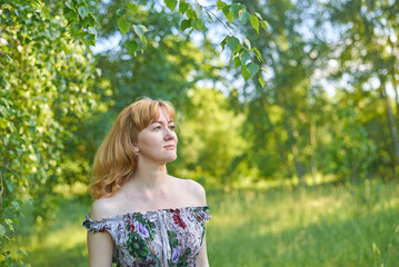 Fototapeta premium A woman is standing in a field wearing a white dress. She is smiling. The field is green and has trees in the background