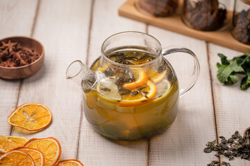 Warm citrus green tea served in a clear glass teapot with fresh orange slices and herbs