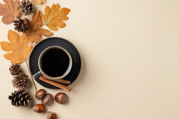 Coffee cup with autumn leaves pine cones nuts and cinnamon sticks arranged on a tan surface