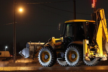 A yellow equal-wheel excavator loader stands on the road at night under a light pole