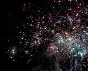 Colorful fireworks exploding in the night sky with smoke trails and bright sparks.