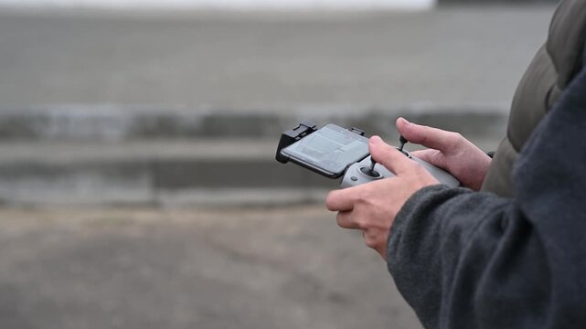 Hands holding a drone remote controller outdoors. Person operating a quadcopter using a handheld transmitter with a smartphone screen.