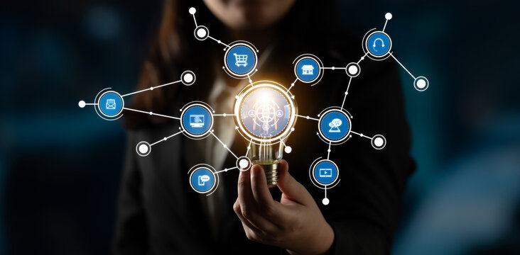 Confident businesswoman presents a light bulb symbolizing innovative ideas with digital connection icons, showcasing modern technology role in business success and strategy. Crux - Powered by Adobe