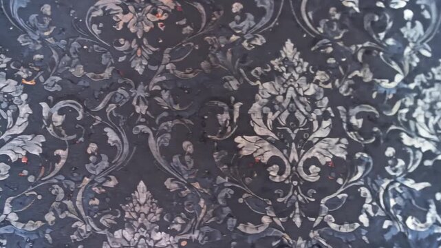 A detailed, close-up shot of a dark-toned surface features an ornate, floral damask pattern