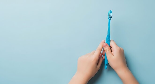 Child hands holding blue toothbrush on light blue background image