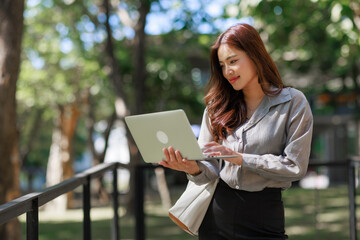 Obraz premium Young asian woman working online standing with laptop outdoors