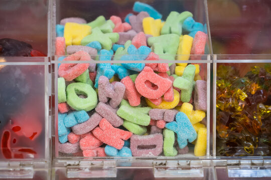Colorful assortment of alphabet-shaped gummy candies displayed in a clear plastic bin at a candy store