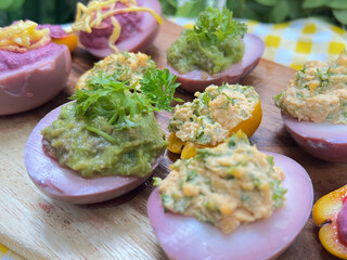 Colorful stuffed eggs and mini bell peppers. The eggs have a pinkish hue and are topped with different fillings, including a green herb mixture, a creamy yellow mixture, and a bright purple spread.