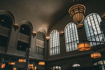 Interior view of a historic building with large arched windows and elegant chandeliers creating a warm atmospheric lighting