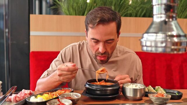 A man enjoys traditional Korean kimchi jjigae soup at a Korean restaurant. Asian food