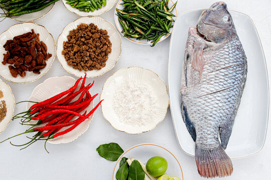 Fresh Whole Tilapia Fish and Cooking Ingredients &ndash; Raw Ikan Nila with Chili, Herbs, Spices, and Seasonings for Asian Cuisine, Top View Food Preparation Photography