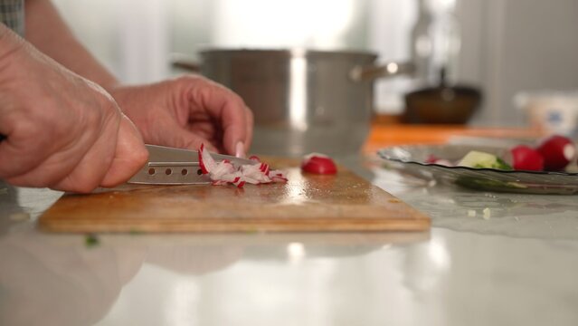 Chef slicing fresh radishes on wooden cutting board