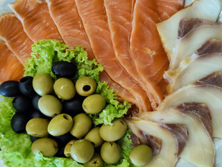 Sliced fish with green and black olives and lettuce. Restaurant service. Top view.