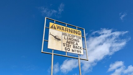 Old vintage warning sign helicopter landing area stay back 60 metres against sunny blue sky 