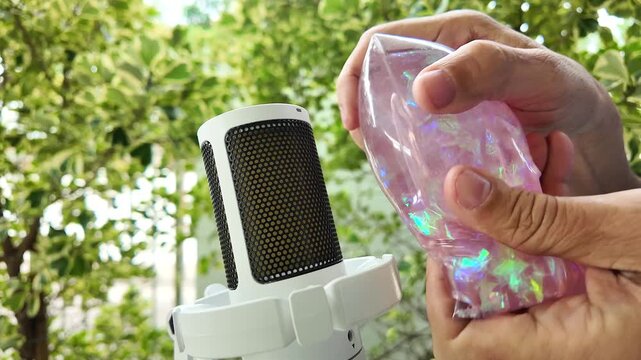 ASMR squishing sound. Hands squeezing pink glitter slime bag near mic.