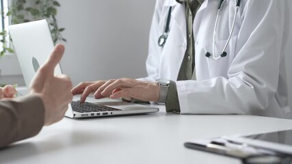Doctor wearing lab coat and stethoscope typing on laptop keyboard and explaining something to patient during a medical consultation in hospital office. Medicine and health care concept - Powered by Adobe